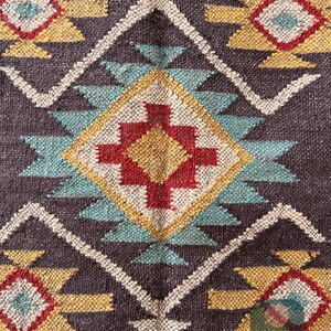 May include: Close-up of a brown woven rug with a geometric pattern in shades of red, yellow, blue, and white. The pattern features triangles, diamonds, and squares.