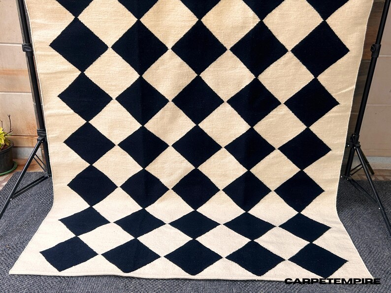 Elevate your space with this Modern Wool Rug, a handwoven geometric check design that blends timeless craftsmanship with minimalistic Scandi style. Featuring a black and white diamond checkered pattern, this flatweave rug is crafted from 100% natural wool, making it both soft and durable