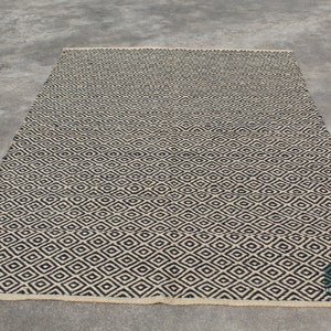 May include: A black and white diamond patterned rug with a woven texture. The rug has a natural fibre look and feel.