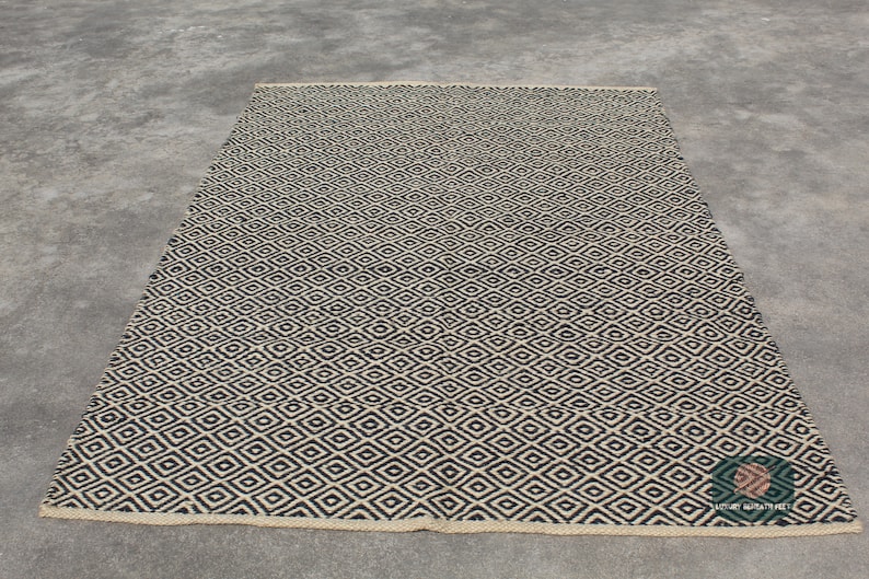 May include: A black and white diamond patterned rug with a woven texture. The rug has a natural fibre look and feel.