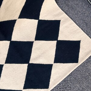 Modern Scandi-style wool rug with black and white diamond check motifs. Handcrafted by artisans using traditional techniques, this durable flatweave rug enhances the aesthetic of modern homes, adding warmth and structure to minimalist spaces.
