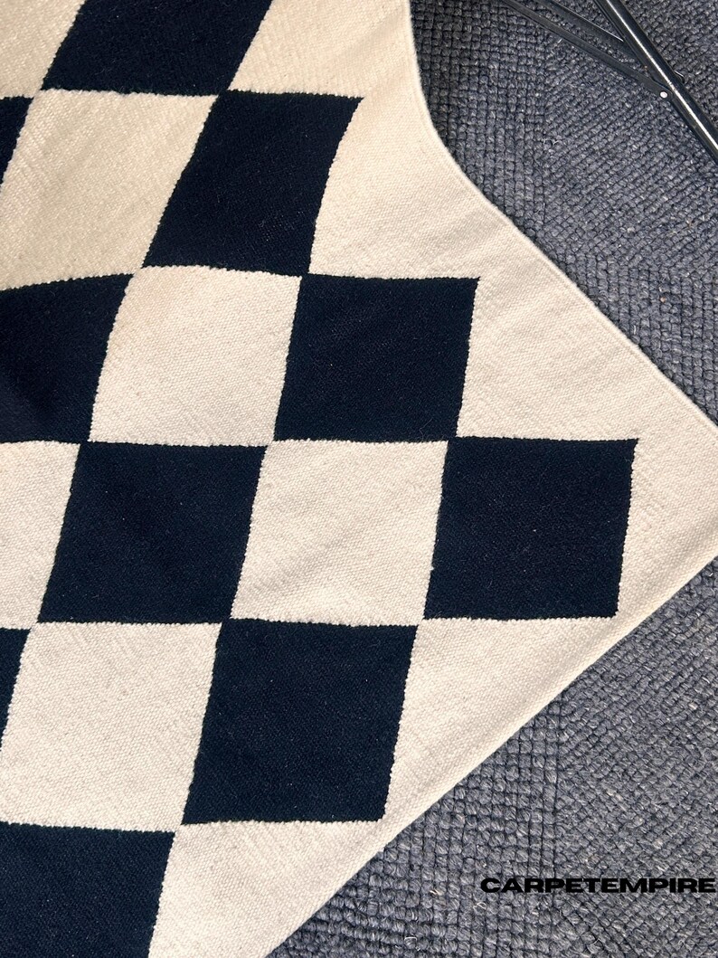 Modern Scandi-style wool rug with black and white diamond check motifs. Handcrafted by artisans using traditional techniques, this durable flatweave rug enhances the aesthetic of modern homes, adding warmth and structure to minimalist spaces.