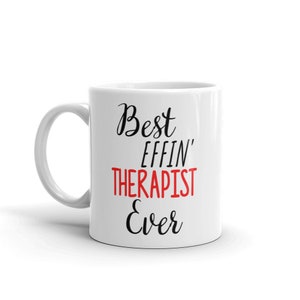 May include: White ceramic coffee mug with black text that reads "Best Effin' Therapist Ever". The word "Therapist" is in red.
