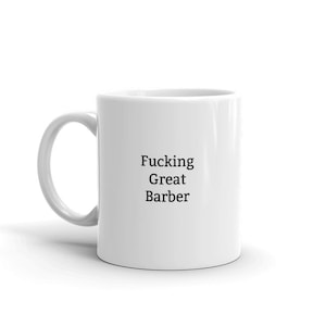 Op de afbeelding: Witte keramische koffiemok met zwarte tekst die "Fucking Great Barber" luidt.