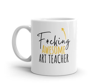 May include: White ceramic coffee mug with a black and gold design. The text on the mug reads "F*cking Awesome Art Teacher" with an arrow pointing upwards.