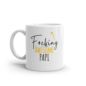Może przedstawiać: Biały ceramiczny kubek do kawy z czarnym i złotym wzorem. Tekst na kubku brzmi "F*cking Awesome Papi" ze strzałką skierowaną w górę.
