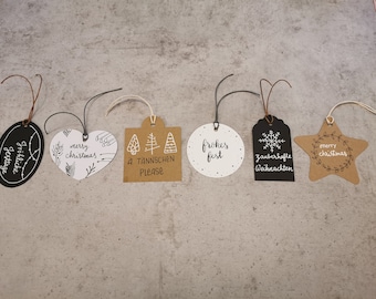Könnte beinhalten: Sechs verschiedene Weihnachtsgeschenkanhänger mit unterschiedlichen Designs und Texten. Die Anhänger sind aus braunem Papier und haben weiße Tinte. Die Designs beinhalten ein Herz, einen Stern, eine Schneeflocke, einen Kreis und zwei Anhänger mit Weihnachtsbäumen. Der Text auf den Anhängern lautet "Merry Christmas", "Frohe Feiertage", "Frohes Fest", "A Tannenchen Please", "Zauberhafte Weihnachten" und "Merry Christmas".