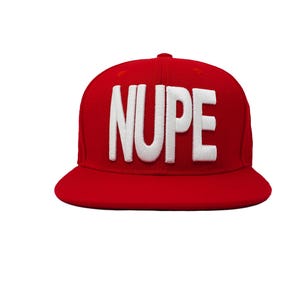 May include: A bright red baseball cap featuring the word NUPE embroidered in large, bold, white capital letters across the front panel. The hat has a structured crown and a flat brim, maintaining a consistent solid red color throughout the design.