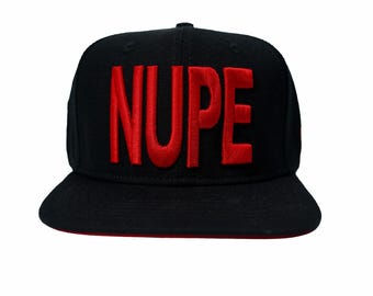 May include: A black baseball cap featuring the word NUPE embroidered in bold red capital letters across the front panel. The hat has a structured crown and a flat brim with a red underside, providing a clear view of the front design.