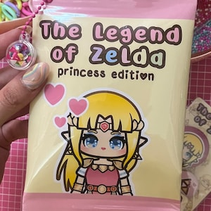 Peut inclure: Un sac en plastique rose et jaune avec une image de dessin animé de la princesse Zelda de la série de jeux vidéo The Legend of Zelda. Le sac porte l'inscription "The Legend of Zelda princess edition".