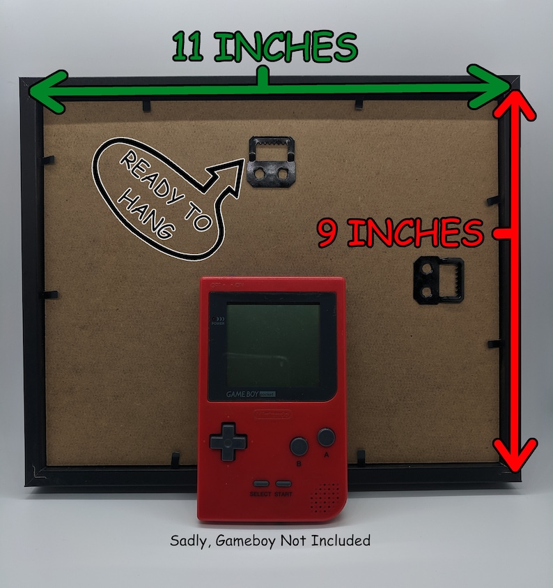 May include: Black picture frame, 28 cm wide and 23 cm tall, with a brown backing. Includes a red Game Boy and the text "READY TO HANG". The text "Sadly, Gameboy Not Included" is also present.
