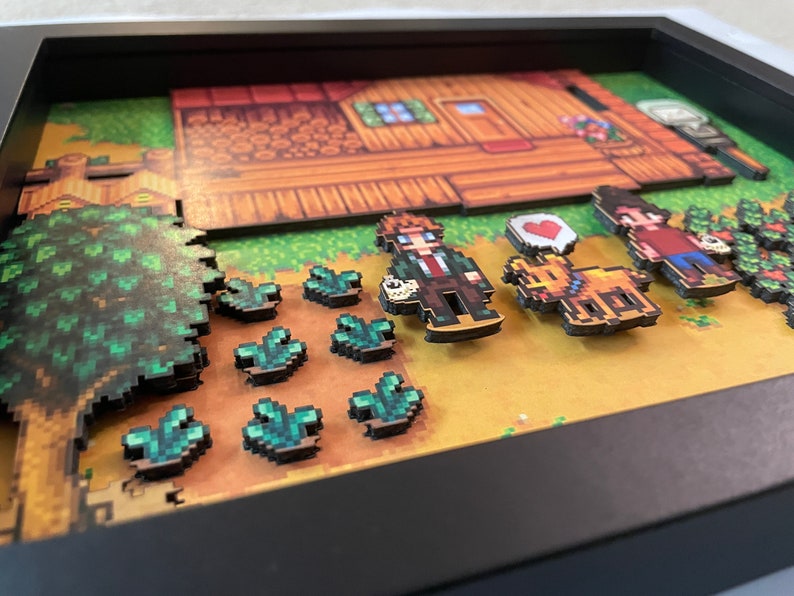 May include: A framed artwork featuring a pixelated farm scene with characters, crops, and a house. The piece includes a brown house, green crops, and characters with a heart symbol. The color scheme is dominated by brown, green, and yellow.