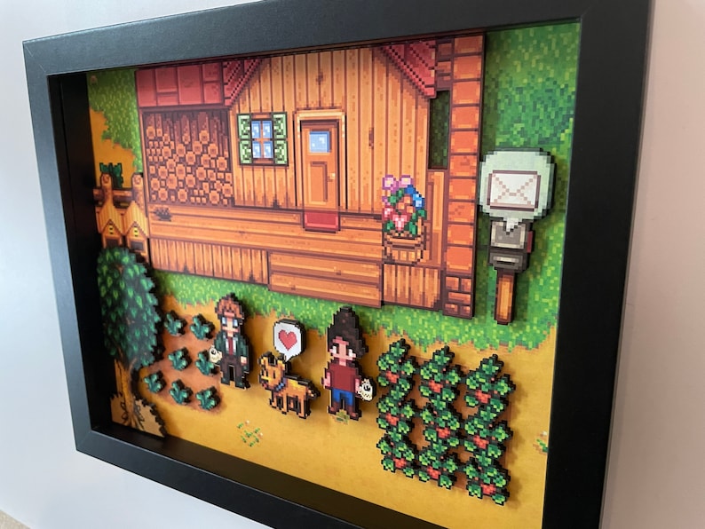 May include: A framed pixel art scene showing a wooden house with a red roof, a mailbox, and characters in a field. The art features a dog with a heart, crops, and a tree. The artwork is in a black frame.