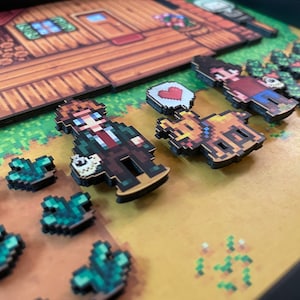 May include: A framed pixel art diorama depicting characters and elements from a video game. The scene includes a wooden house, characters, a bear, and crops. The characters are in a pixelated style, with a heart symbol. The color palette is dominated by browns, greens, and yellows.
