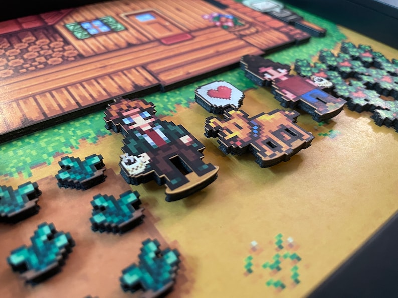 May include: A framed pixel art diorama depicting characters and elements from a video game. The scene includes a wooden house, characters, a bear, and crops. The characters are in a pixelated style, with a heart symbol. The color palette is dominated by browns, greens, and yellows.
