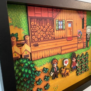 May include: A framed pixel art diorama depicting a wooden house with a door, window, and mailbox. The artwork includes characters, crops, and a dog, all in a retro video game style. The frame is black.