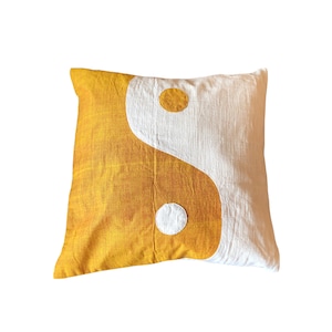 Op de afbeelding: Een geel en wit kussen met een yin yang symbool.