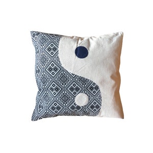Op de afbeelding: Een wit en blauw gepatroneerd kussen met een yin yang-ontwerp. Het yin yang-symbool bestaat uit twee cirkels, een witte en een zwarte, die met een lijn zijn verbonden. Het kussen is gemaakt van een zachte, comfortabele stof.