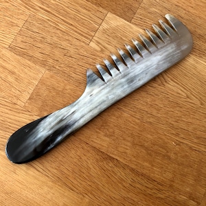 Peut inclure: Un peigne en corne noir et blanc avec un design à dents larges. Le peigne a une poignée arrondie et est fait de corne naturelle.