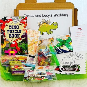 May include: A gift box filled with dinosaur-themed party favors. Includes a puzzle book, crayons, stickers, and other small toys. The box is decorated with a dinosaur illustration and the text "James and Lucy's Wedding".
