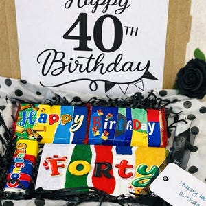 May include: A cardboard gift box containing chocolate bars with colorful wrappers. The box lid features the text Happy 40th Birthday. Inside, chocolate bars display the words Happy Birthday and Forty, with a small bar labeled Congrats.