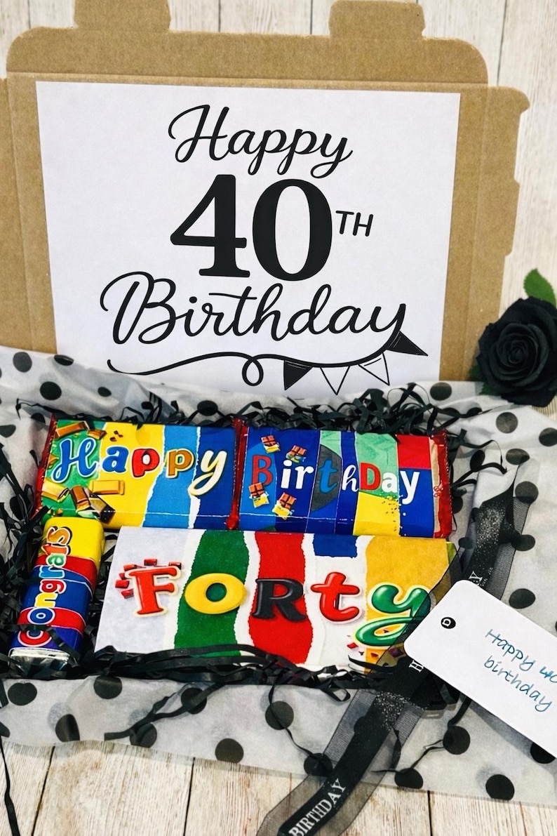 May include: A cardboard gift box containing chocolate bars with colorful wrappers. The box lid features the text Happy 40th Birthday. Inside, chocolate bars display the words Happy Birthday and Forty, with a small bar labeled Congrats.