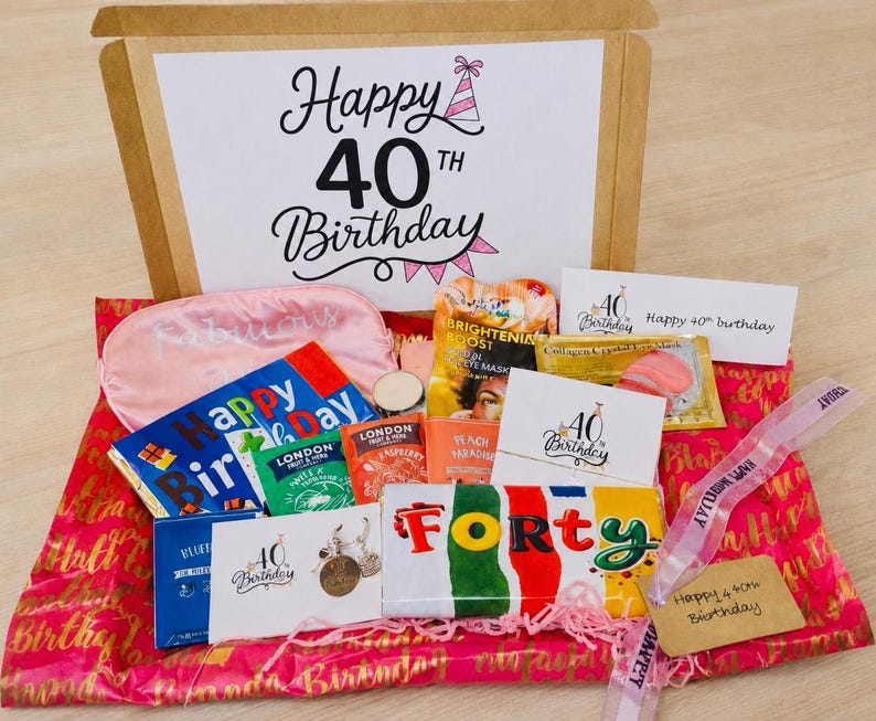 May include: A 40th birthday gift box containing a pink sleep mask, various tea packets, a chocolate bar labeled FORTY, a card with the text Happy 40th Birthday, and a small metal charm, all arranged on pink wrapping paper with gold text.