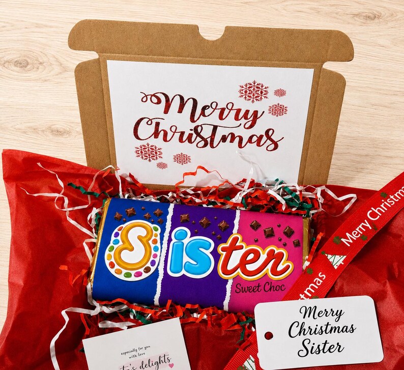 May include: A brown cardboard gift box containing a chocolate bar with a wrapper that reads Sister Sweet Choc. The box lid features the text Merry Christmas in red. Included are red tissue paper, a red ribbon, and a white gift tag reading Merry Christmas Sister.