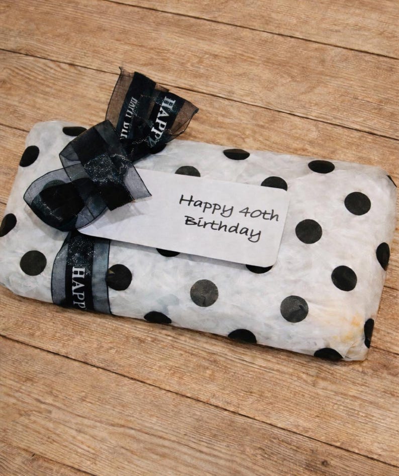 May include: A rectangular gift wrapped in white tissue paper with black polka dots, tied with a black sheer ribbon featuring the text "HAPPY BIRTHDAY" in white, and a white gift tag with the handwritten text "Happy 40th Birthday".
