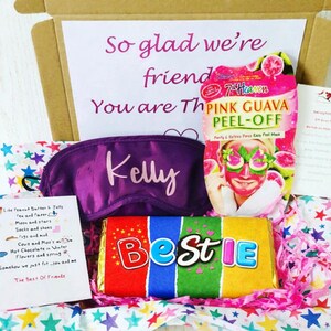 May include: A gift box filled with self-care items. It includes a purple eye mask with the name "Kelly", a pink guava peel-off face mask, and a colorful candy bar that says "Bestie". The box also contains a handwritten note.