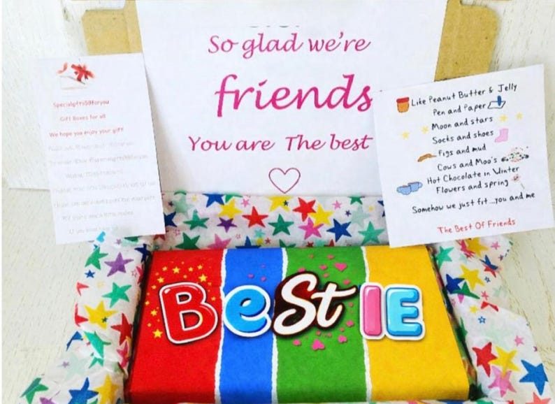 May include: A gift box with a colorful "Bestie" candy bar and handwritten notes. The box contains a candy bar with red, blue, green, and yellow sections. The notes say "So glad we're friends" and list various items like peanut butter and jelly.