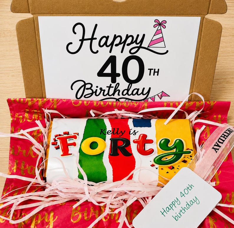 May include: A cardboard gift box containing a chocolate bar wrapped in colorful paper with the text Kelly is FORTY. The box lid features the text Happy 40TH Birthday with a party hat icon. Pink shredded paper filler and a Happy 40th birthday tag.