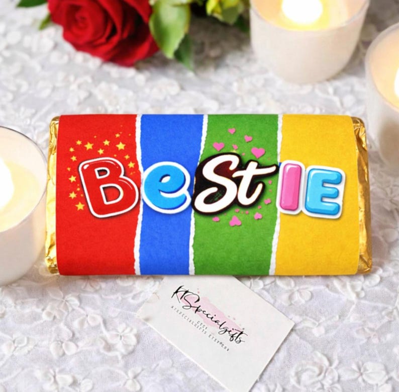 May include: A colorful candy bar wrapper with the word "Bestie" in a playful font. The wrapper is divided into red, blue, green, and yellow sections. Small hearts and stars decorate the design. A small white card with text is in the foreground.