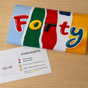 May include: A rectangular candy bar wrapper featuring the word Forty in colorful, rounded 3D letters against a background of vertical, torn-paper style stripes in light blue, green, red, and yellow. A white business card with KTSPECIALGIFTS text.