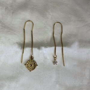 May include: A pair of gold dangle earrings. One earring features a small star charm, while the other has a larger, intricate, circular charm.