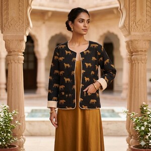 May include: A black quilted jacket featuring a gold tiger print, cream trim, and lining. The jacket is worn over a mustard dress. The jacket has two pockets and is open at the front. The jacket's length is approximately 60 cm.