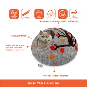 Pode incluir: Uma cama para gatos de feltro cinza em forma de cúpula com um design de árvore e detalhes em feltro laranja e vermelho. Um gato está sentado dentro da cama. A cama é feita de 100% lã de ovelha da Nova Zelândia.