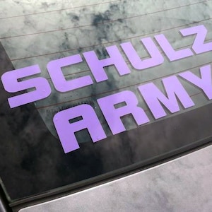 Pode incluir: Um adesivo de vinil roxo na janela de um carro que diz "SCHULZ ARMY".