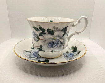 May include: A white teacup and saucer set featuring a blue and white floral design. The cup has a dainty handle and the saucer has a scalloped rim.