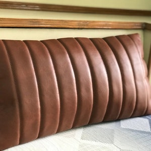May include: A brown leather cushion with a quilted design. The cushion is rectangular and has a soft, plush texture.