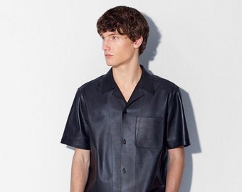 Può includere: Una camicia in pelle nera a maniche corte con chiusura a bottoni e una tasca sul petto sinistro.
