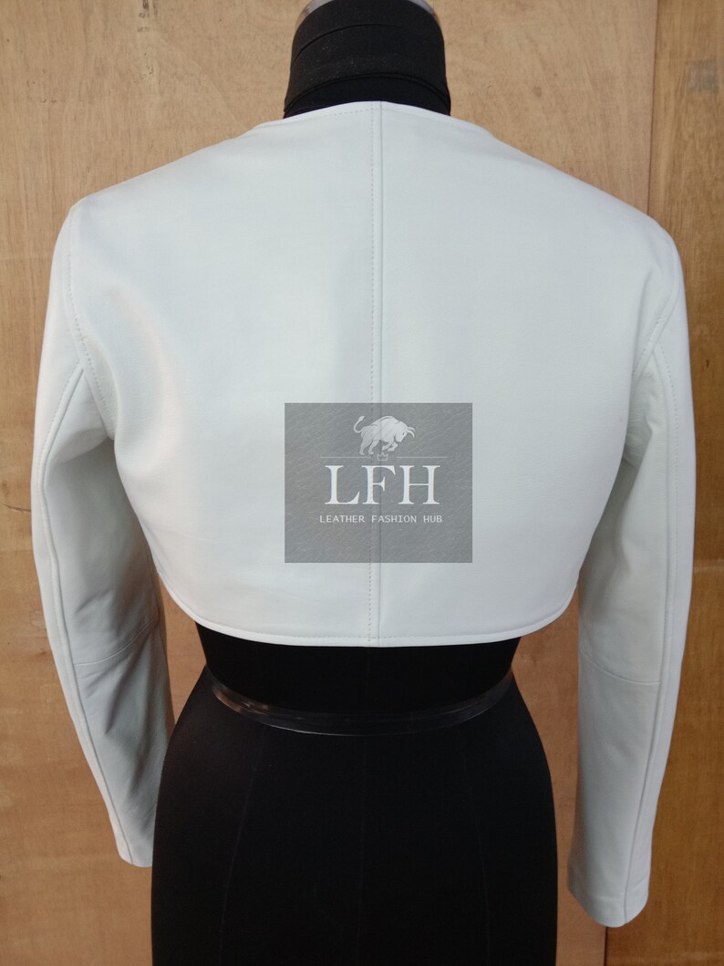 May include: A white cropped leather jacket with long sleeves. The jacket has a simple design and is made of soft, supple leather. The jacket is shown on a mannequin with a black skirt.