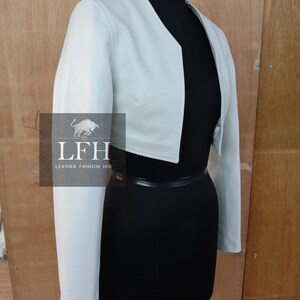 May include: A light blue cropped leather jacket with long sleeves. The jacket is on a mannequin with a black skirt and a black belt.