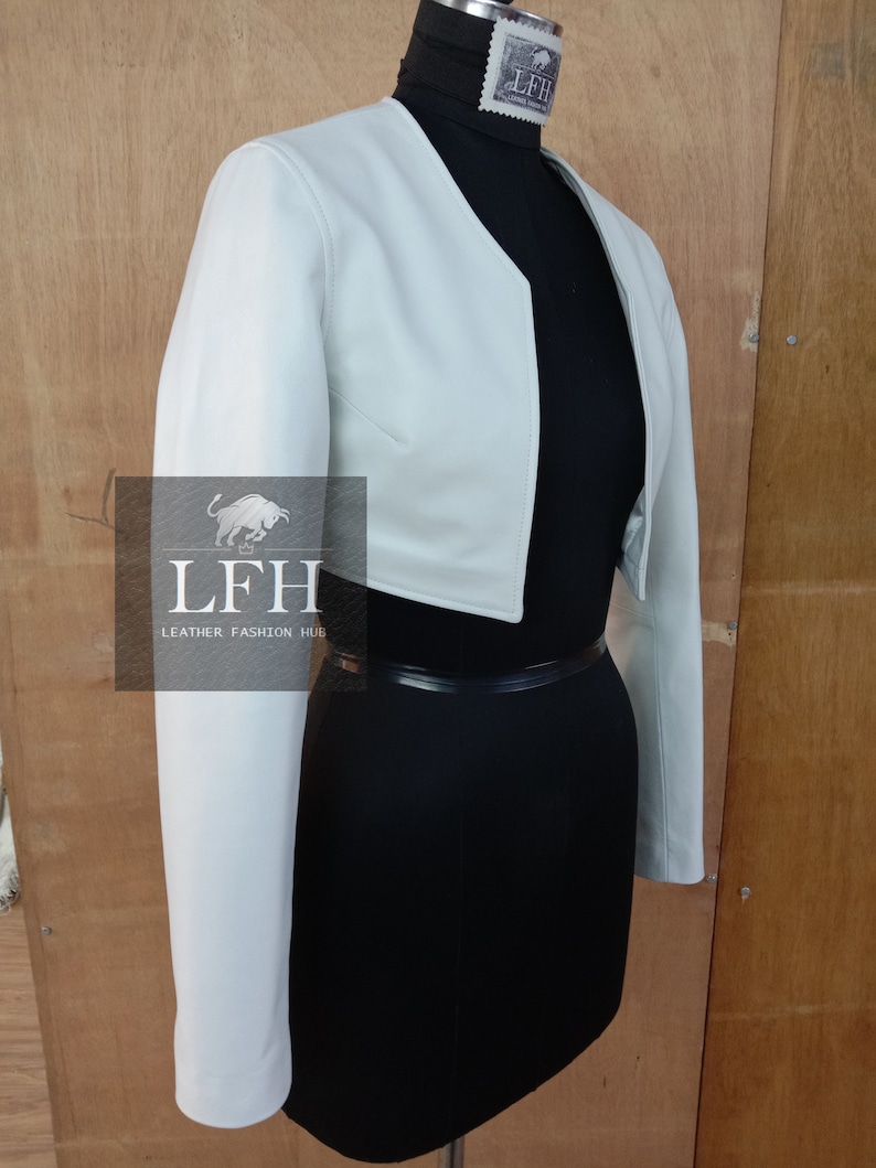 May include: A light blue cropped leather jacket with long sleeves. The jacket is on a mannequin with a black skirt and a black belt.