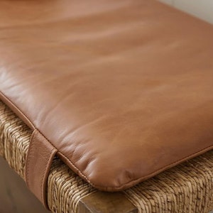 May include: A brown leather cushion with a woven base. The cushion is thick and has a stitched edge.