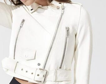 May include: Cream-colored, cropped motorcycle jacket with silver zippers and a belted waist. The jacket features a classic asymmetrical design with a small pocket and a notched collar. The sleeves have zippers at the cuffs.
