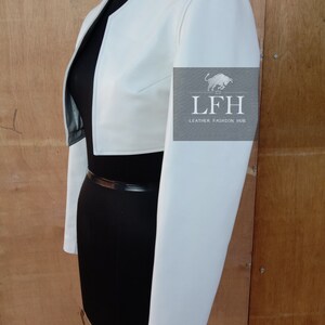May include: A white cropped leather jacket with long sleeves. The jacket has a simple design and is made of a soft, supple leather. The jacket is shown on a black mannequin.