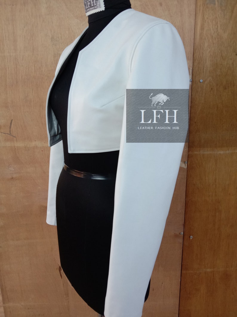 May include: A white cropped leather jacket with long sleeves. The jacket has a simple design and is made of a soft, supple leather. The jacket is shown on a black mannequin.