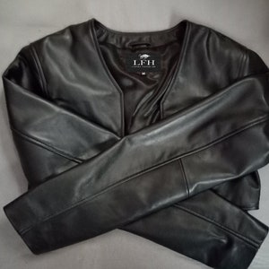 May include: A black leather jacket with a V-neck and long sleeves. The jacket has a small label on the front that says "LFH".