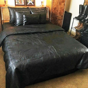 May include: A black leather bedspread with a quilted design. The bedspread is on a bed with black leather pillows.